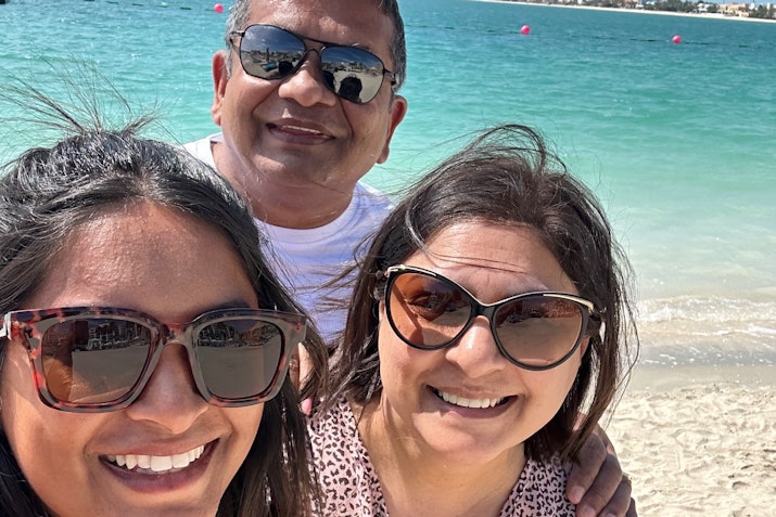 A group of three people smiling at the beach, wearing sunglasses.