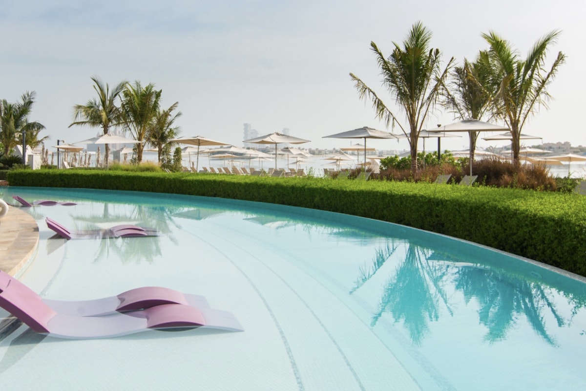 W Dubai Palm Jumeirah A serene pool area with purple lounge chairs set against a backdrop of umbrellas and lush greenery.