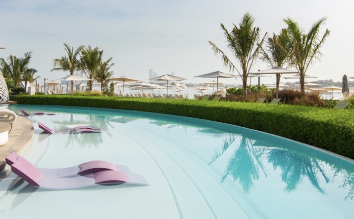 A serene pool area with purple lounge chairs set against a backdrop of umbrellas and lush greenery.