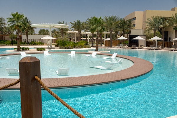 Pool area with lounge chairs placed in a circular arrangement surrounded by palm trees and umbrellas.