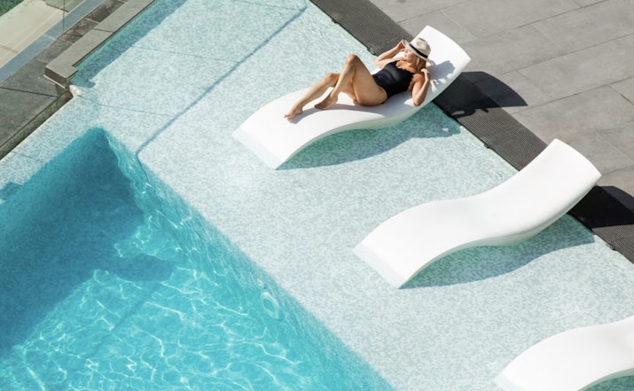 InterContinental Dubai Marina A person relaxing by the pool on a white lounge chair, wearing a black swimsuit and a hat.