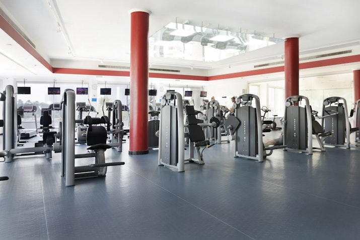 Bright gym with various exercise machines, featuring red columns and large windows for natural light
