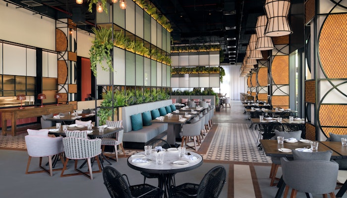 Mövenpick Resort Al Marjan Island An elegant restaurant interior featuring modern furniture, lush greenery, and artistic light fixtures, creating a chic dining atmosphere.