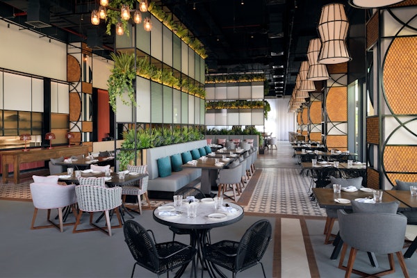 An elegant restaurant interior featuring modern furniture, lush greenery, and artistic light fixtures, creating a chic dining atmosphere.