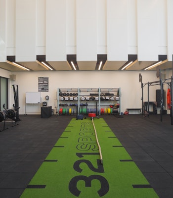 321 Sports A spacious gym with a green workout track in the center, surrounded by exercise equipment like rowing machines, weights, and functional training gear.