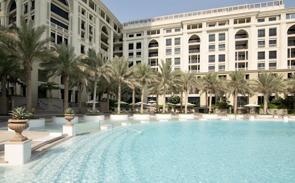A luxurious swimming pool with gentle slopes, surrounded by palm trees and elegant resort architecture.