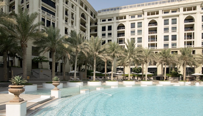 Palazzo Versace Dubai Elegant poolside area with palm trees and a luxury hotel building in the background.