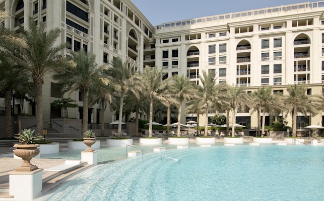 Elegant poolside area with palm trees and a luxury hotel building in the background.