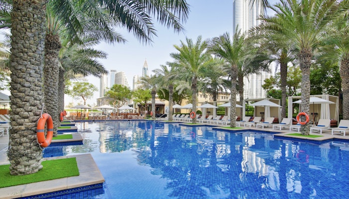 The Palace Downtown Dubai   A pool surrounded by palm trees and loungers, with a view of city skyscrapers in the background.