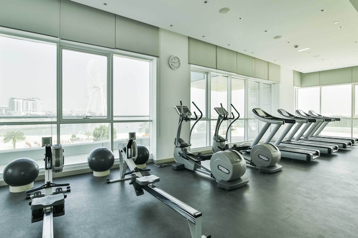 A spacious gym filled with exercise equipment, including elliptical machines and weights, featuring large windows with a view