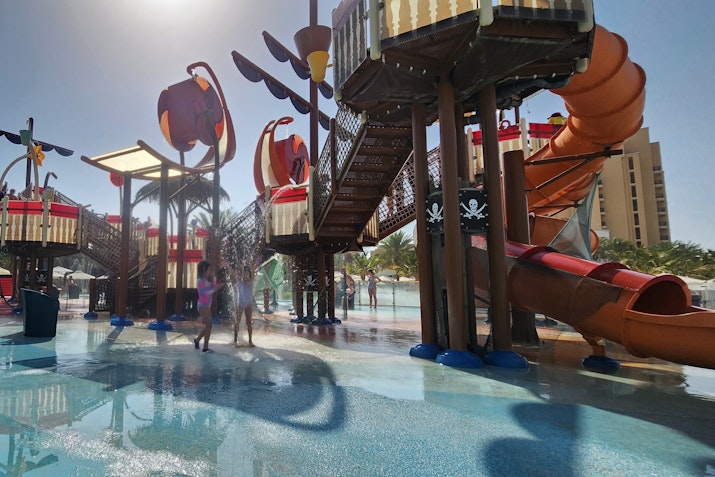 A vibrant water play area featuring pirate-themed slides and structures with children playing in the water.