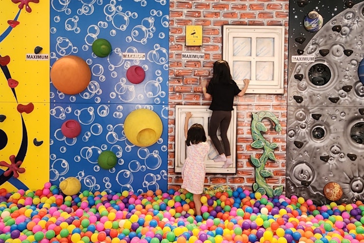 Chuckles Kids' Club A child playing in a colorful ball pit surrounded by vibrant, themed wall decorations.