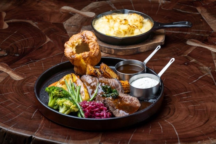 Sneak peek of a delicious roast meal with Yorkshire pudding, vegetables, and sauces.