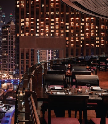 Asia Asia, Dubai Marina Elegant outdoor dining overlooking a marina at night with city lights and boats in view.