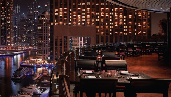 Asia Asia, Dubai Marina Elegant outdoor dining overlooking a marina at night with city lights and boats in view.