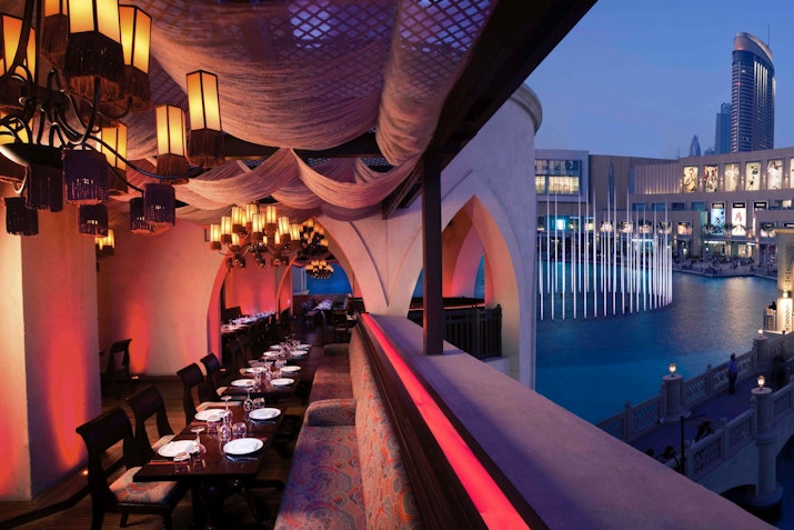 Karma Kafé restaurant at Souk Al Bahar, with outdoor seating overlooking Dubai Fountain, featuring elegant lantern lighting, draped canopies, and a vibrant evening ambiance.