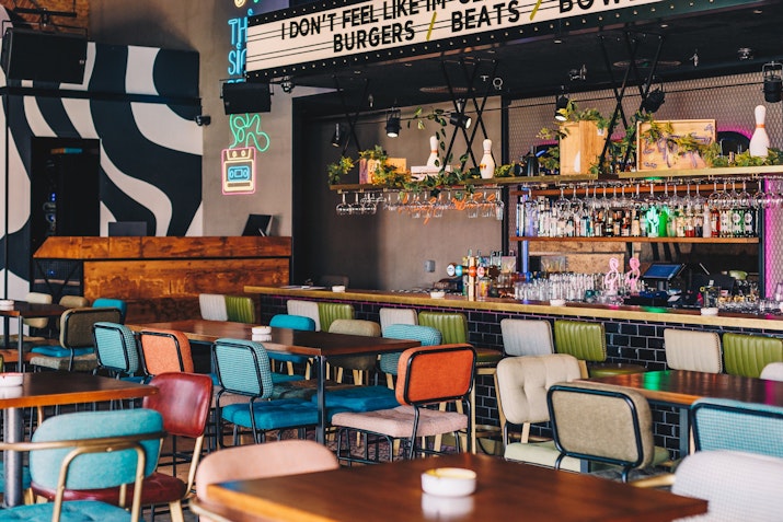 Trendy bar with colorful seating, neon signs, and a vibrant drink selection behind the counter