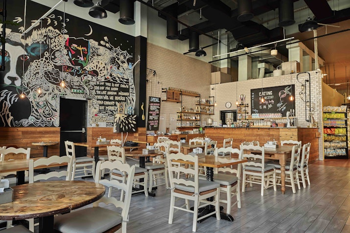 Trendy restaurant interior with eclectic wall art, wooden tables, and white chairs, creating a casual dining atmosphere.