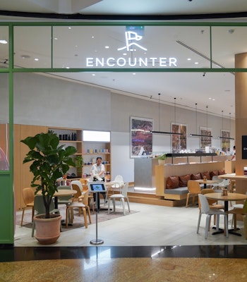 Encounter Coffee Roasters Modern café entrance with green-framed glass walls, minimalist decor, and 'Encounter' sign above, showing seating area inside.