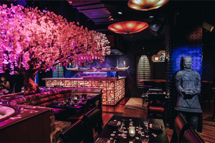 Asian-themed restaurant interior with a pink blossom tree, traditional statues, and dim ambient lighting.