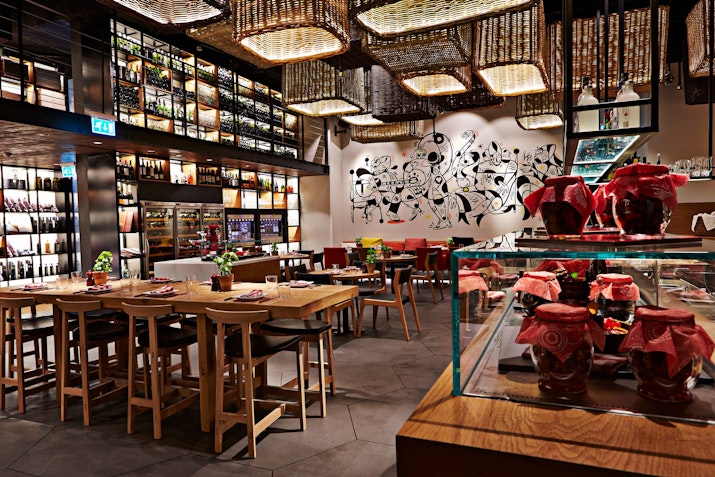 Contemporary restaurant with wooden tables, artistic wall mural, hanging woven baskets, and preserved jars on display