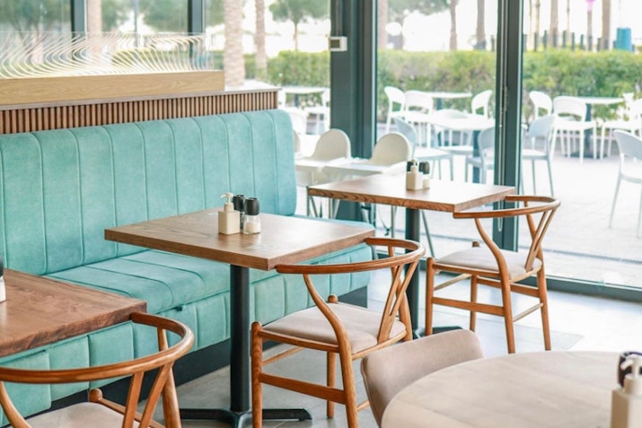 Wooden tables with stylish chairs and teal bench seating in a bright café setting