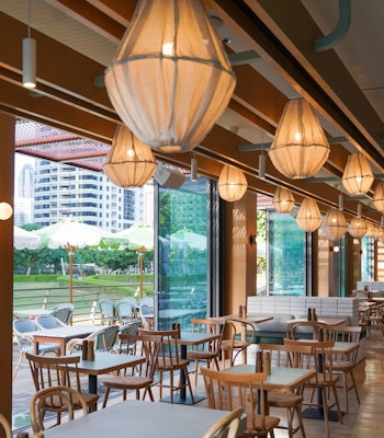 Splendour Fields A restaurant featuring large floor to ceiling windows, natural light and wooden seating with unique lighting overhead overlooking lush greenery
