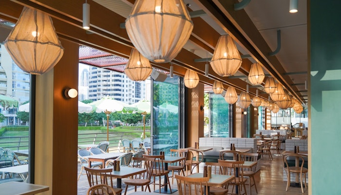Splendour Fields A restaurant featuring large floor to ceiling windows, natural light and wooden seating with unique lighting overhead overlooking lush greenery