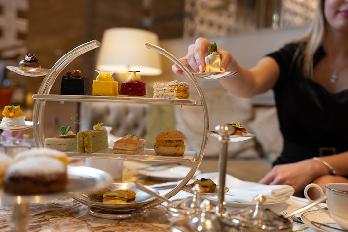 A person reaching for a dessert from an elegant three-tiered cake stand with colorful pastries