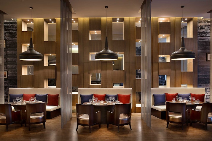 Upscale restaurant interior featuring modern lighting, plush seating, and stylish wooden partition walls.