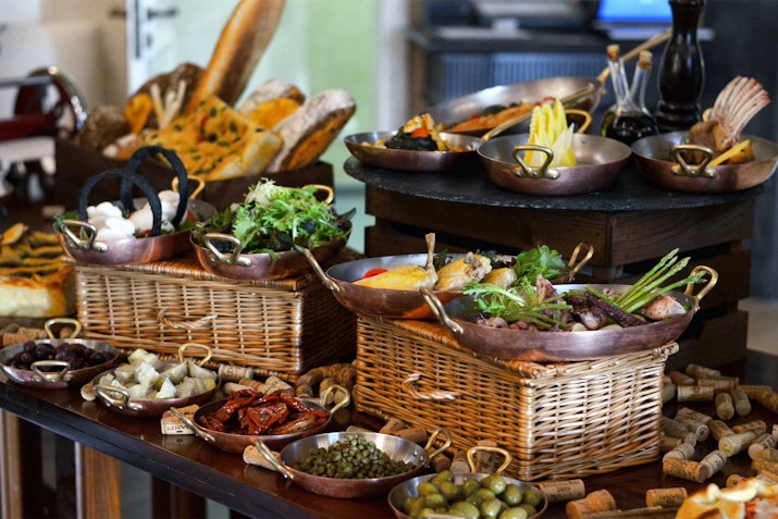 A beautifully arranged brunch table with baskets of bread, herbs, and a variety of fresh ingredients.