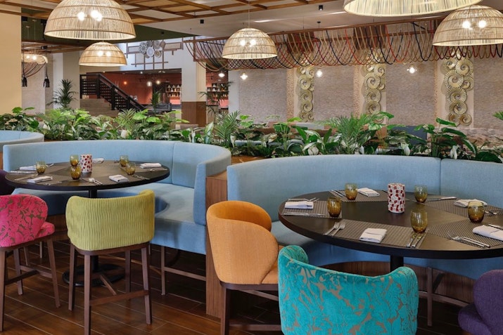 Colorful restaurant seating area with plants and pendant lights.