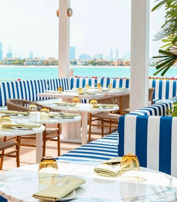 Villamore, Kempinski Hotel & Residences Palm Jumeirah Outdoor restaurant seating area with blue and white striped cushions and a view of the city skyline.