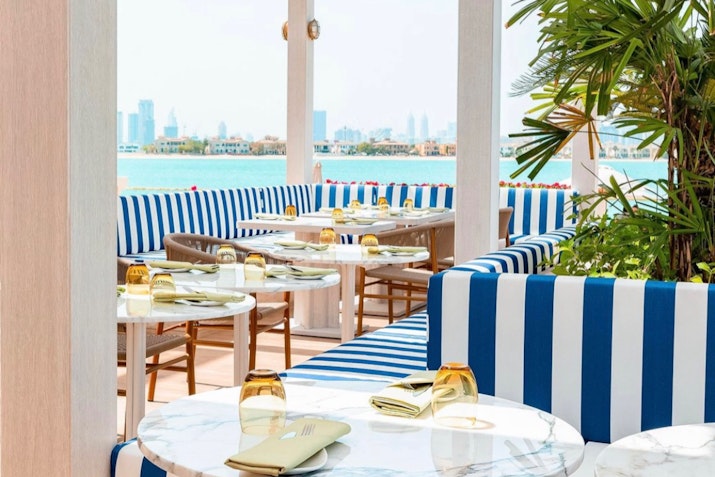 Outdoor restaurant seating area with blue and white striped cushions and a view of the city skyline.