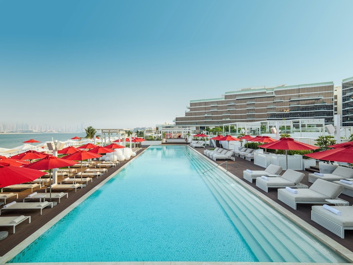 Large pool with red umbrellas and sun loungers, overlooking the sea.