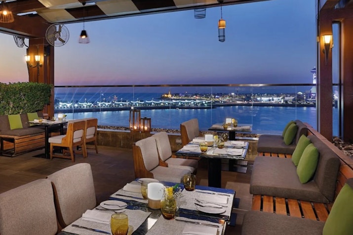 Outdoor restaurant seating with a view of the city skyline at dusk, with tables set for dining.