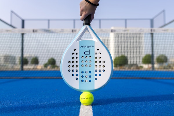 Padel racket and ball on a blue court.