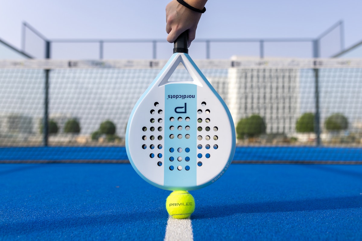 Padel racket and ball on a blue court.