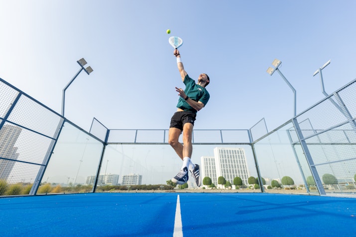 Person hitting a ball with a padel racket on a blue padel court.