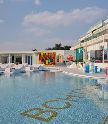 BCH:CLB Pool area with white loungers, colorful decor, and modern building in the background.