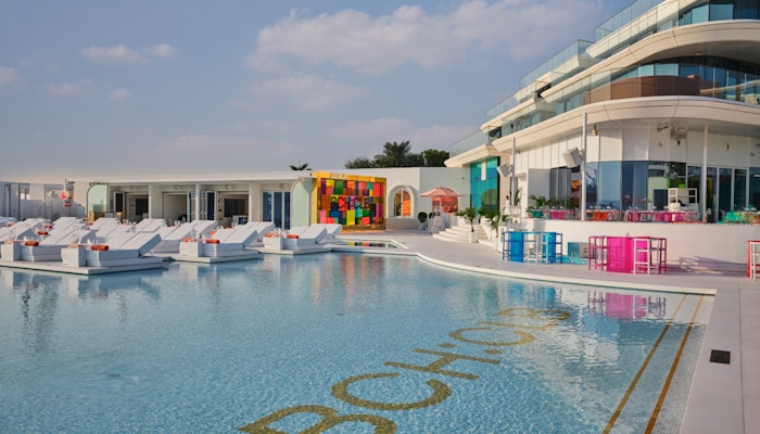BCH:CLB Pool area with white loungers, colorful decor, and modern building in the background.