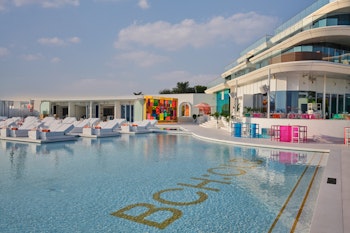 Pool area with white loungers, colorful decor, and modern building in the background.