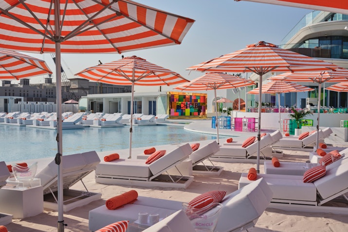 Poolside loungers with red-striped umbrellas and orange towels.