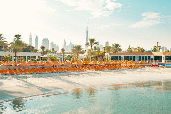 Beach with rows of orange loungers and umbrellas, with city skyline in the background.
