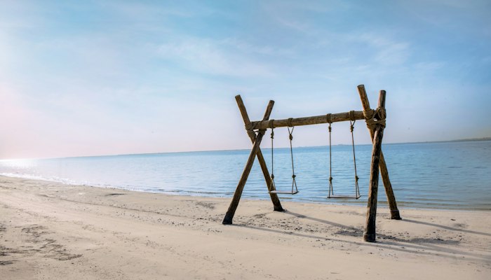 Bab Al Noujoum Wooden swing set on a sandy beach facing calm ocean waters.