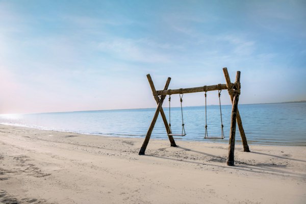 Wooden swing set on a sandy beach facing calm ocean waters.