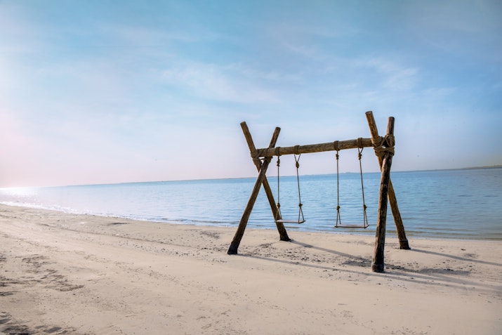 Wooden swing set on a sandy beach facing calm ocean waters.