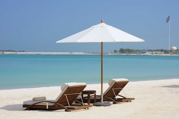 Beach lounge chairs with a white umbrella, overlooking the turquoise sea and a clear sky.