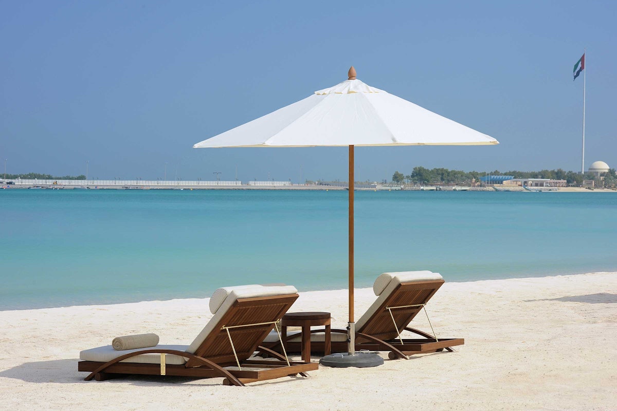 Beach lounge chairs with a white umbrella, overlooking the turquoise sea and a clear sky.