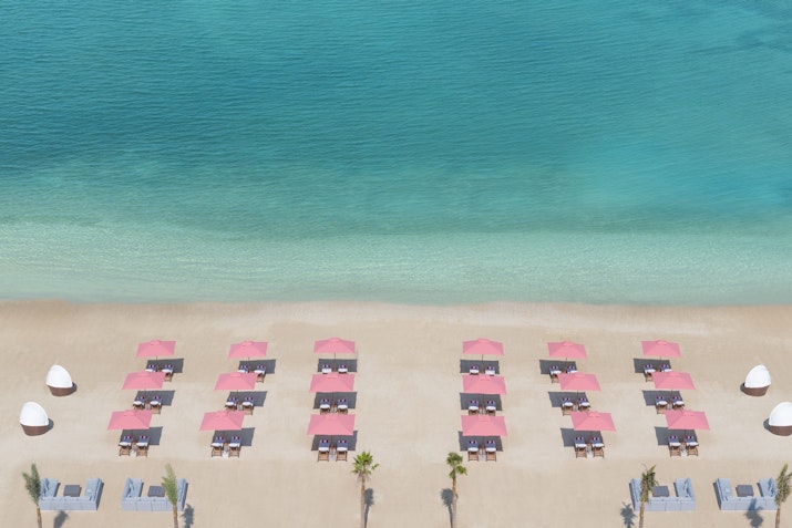 Aerial view of a beach with pink umbrellas and lounge chairs by the turquoise sea.